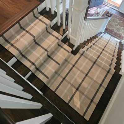 A carpet runner with a plaid pattern of beige, cream, and brown stripes covers a staircase with dark wood treads and white risers.